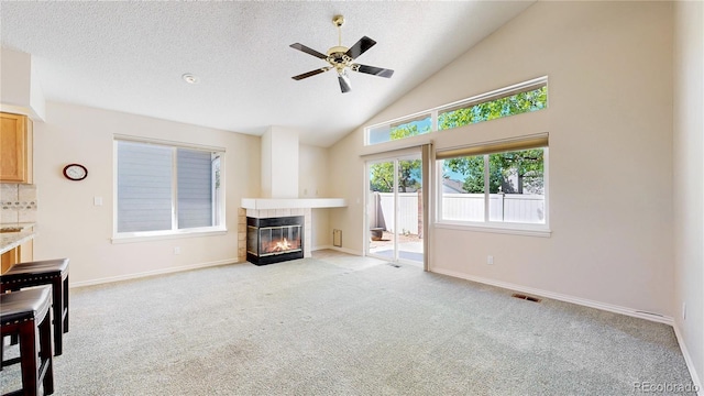unfurnished living room with a tile fireplace, a ceiling fan, light colored carpet, high vaulted ceiling, and baseboards