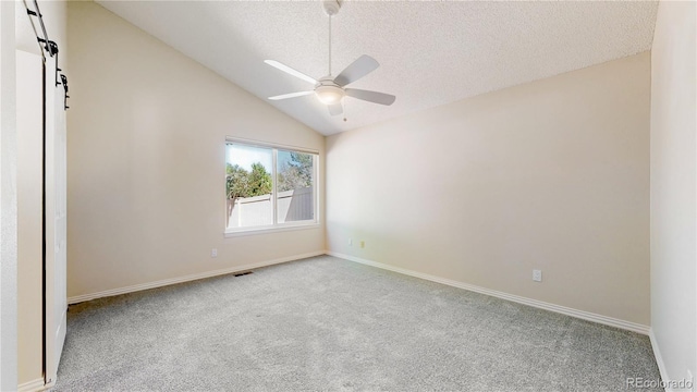 carpeted empty room featuring a barn door, ceiling fan, vaulted ceiling, a textured ceiling, and baseboards