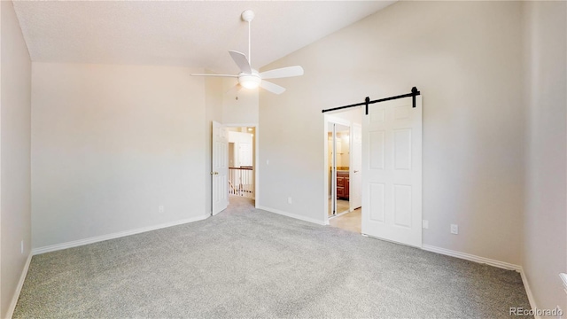 unfurnished bedroom with light carpet, a barn door, baseboards, high vaulted ceiling, and ensuite bath