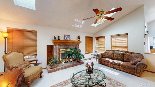 living room featuring carpet, high vaulted ceiling, a brick fireplace, a skylight, and ceiling fan