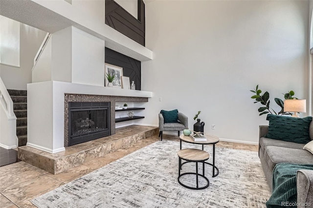 living area featuring baseboards, a high ceiling, a fireplace, and stairs