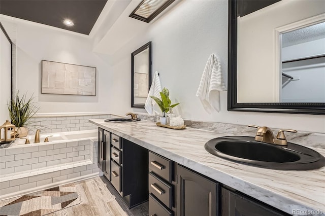 bathroom with double vanity, a sink, a garden tub, and wood finished floors