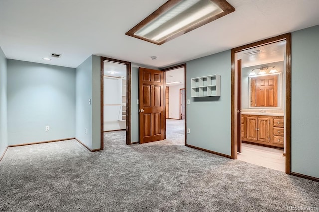 unfurnished bedroom with baseboards, light carpet, connected bathroom, and visible vents