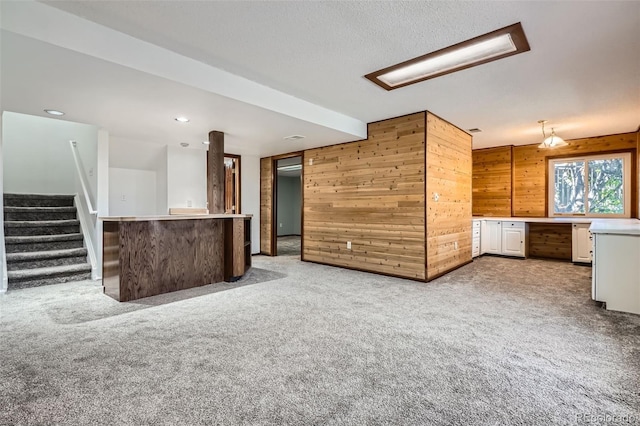 unfurnished living room featuring light colored carpet, built in desk, wood walls, recessed lighting, and stairway