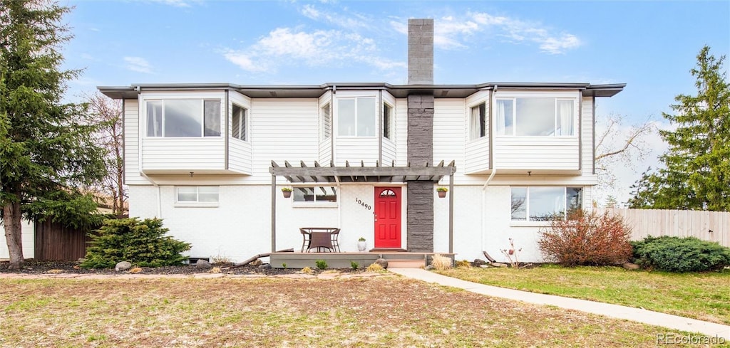 view of front of home featuring a pergola, stucco siding, a front yard, fence, and a chimney