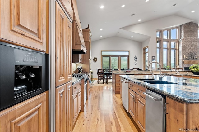 kitchen with appliances with stainless steel finishes, lofted ceiling, sink, dark stone countertops, and light hardwood / wood-style floors