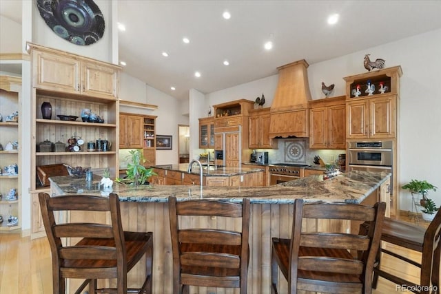 5881 Deer Meadow Trl, Golden, CO 80403 - kitchen with open shelves, custom range hood, a large island with sink, a kitchen bar, and dark stone countertops