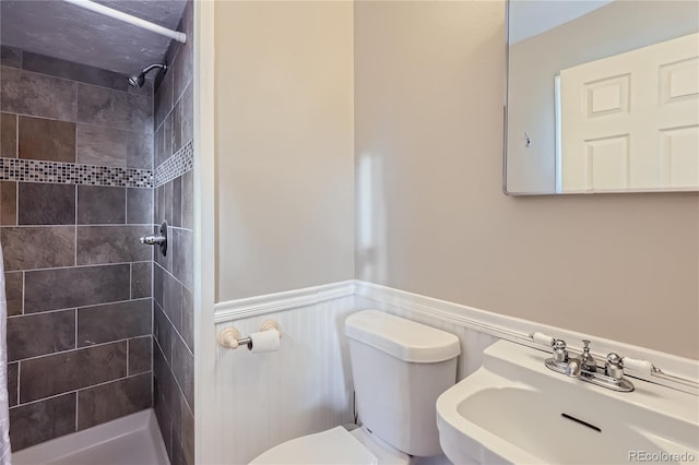 bathroom with tiled shower, toilet, and sink