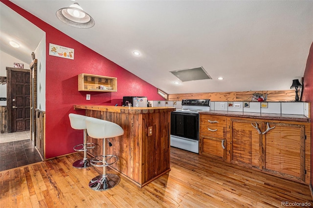 10419 Christopher Dr, Conifer, CO 80433 - kitchen with range with electric stovetop, vaulted ceiling, hardwood / wood-style floors, a peninsula, and a kitchen breakfast bar