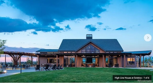 back of property at dusk with a yard, a patio area, board and batten siding, and a chimney