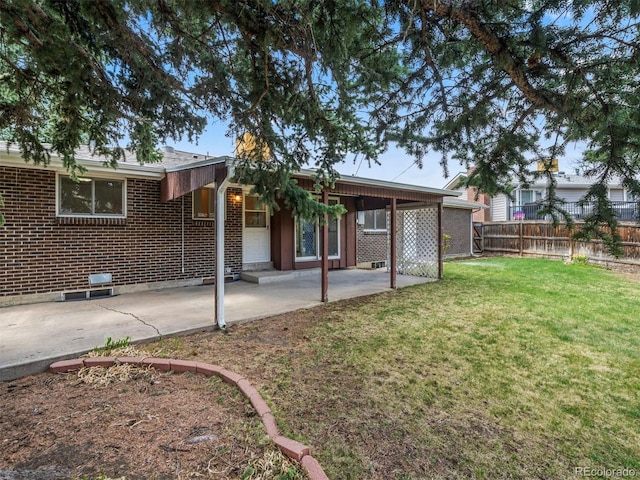 back of house featuring brick siding, a lawn, a patio, and fence