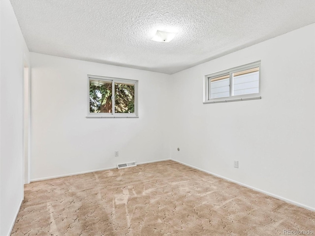 empty room with baseboards, carpet floors, visible vents, and a textured ceiling