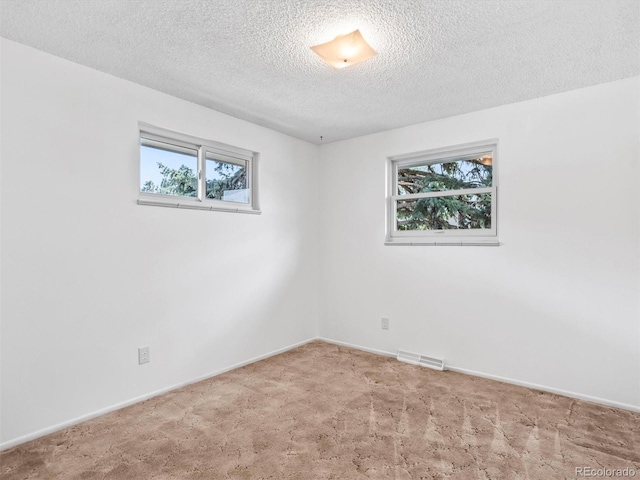 carpeted spare room with baseboards, a textured ceiling, and visible vents