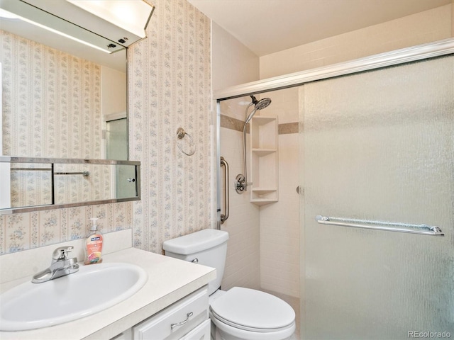 bathroom with wallpapered walls, toilet, vanity, and a stall shower