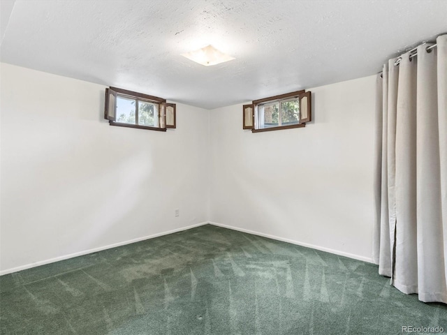 below grade area with baseboards, a healthy amount of sunlight, dark colored carpet, and a textured ceiling