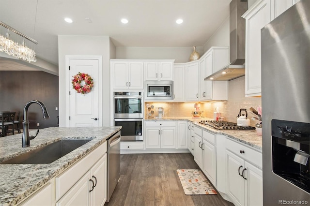 kitchen with a sink, wall chimney range hood, stainless steel appliances, and white cabinetry