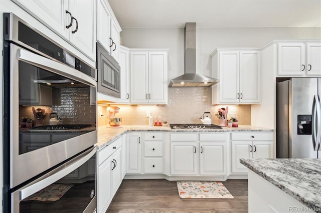 kitchen with wall chimney range hood, dark wood finished floors, light stone counters, stainless steel appliances, and white cabinetry