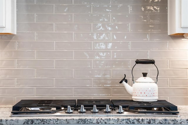 room details featuring backsplash, white cabinets, light stone countertops, and stainless steel gas stovetop