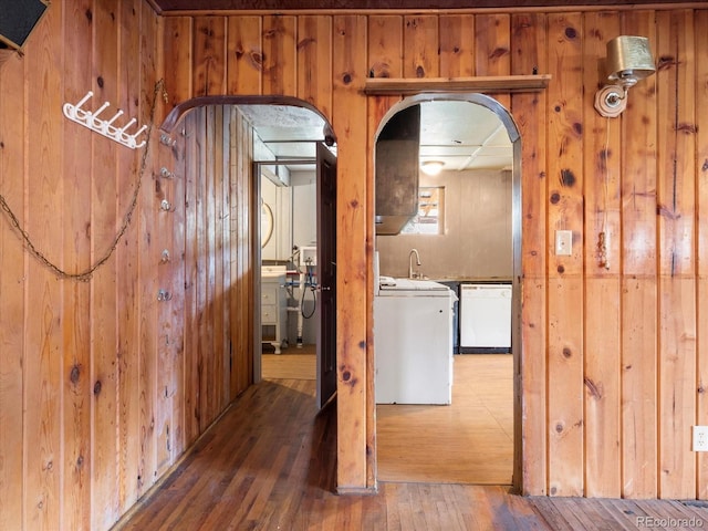 corridor with sink, dark wood-type flooring, and wood walls