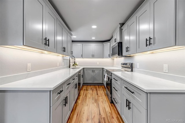 kitchen featuring stainless steel appliances, recessed lighting, light countertops, light wood-style flooring, and a sink