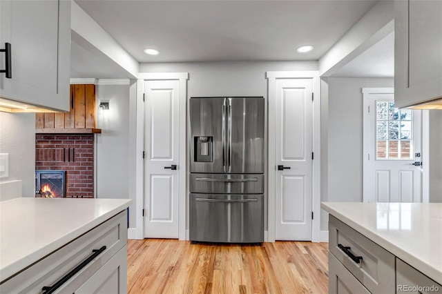 kitchen featuring recessed lighting, a fireplace, light countertops, light wood finished floors, and stainless steel fridge