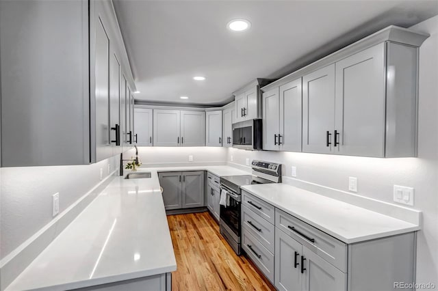 kitchen featuring light wood-style flooring, appliances with stainless steel finishes, light countertops, a sink, and recessed lighting