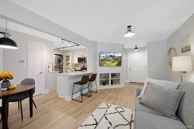 living room with stacked washer and dryer, rail lighting, and light wood-type flooring