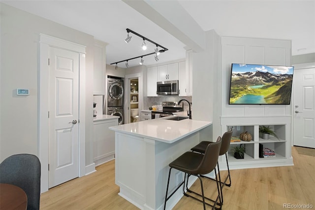 kitchen with appliances with stainless steel finishes, stacked washer and dryer, white cabinetry, and light hardwood / wood-style floors