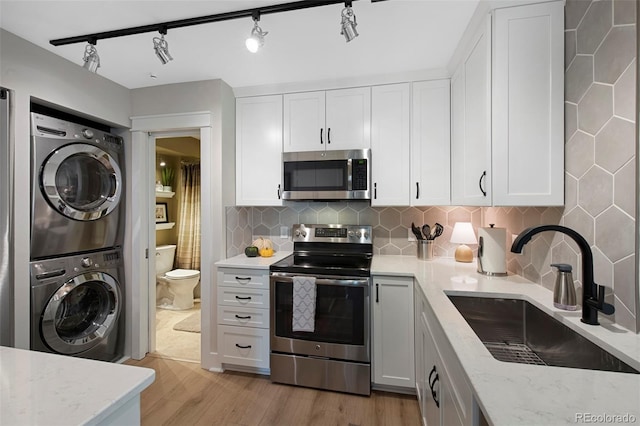 kitchen with appliances with stainless steel finishes, light wood-type flooring, sink, white cabinets, and stacked washer / drying machine