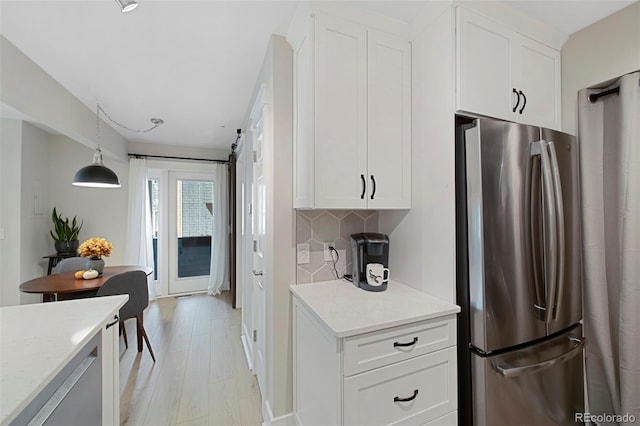 kitchen with stainless steel refrigerator, pendant lighting, decorative backsplash, white cabinets, and light wood-type flooring