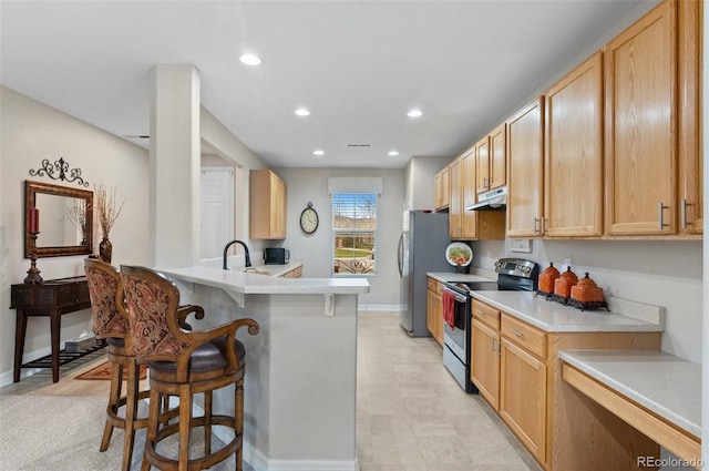 kitchen with baseboards, appliances with stainless steel finishes, under cabinet range hood, and a breakfast bar