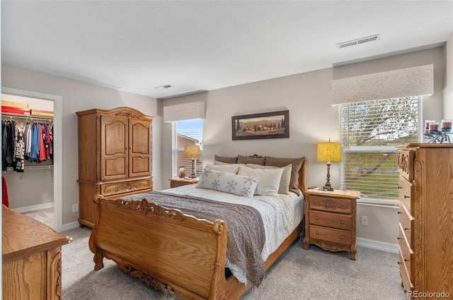 bedroom featuring baseboards, visible vents, light carpet, and a walk in closet