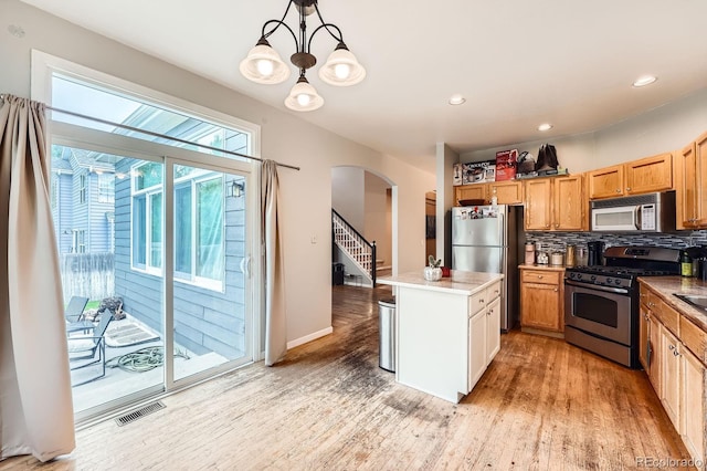 5136 S Ceylon St, Centennial, CO 80015 - kitchen with stainless steel appliances, arched walkways, light wood-style flooring, a center island, and backsplash