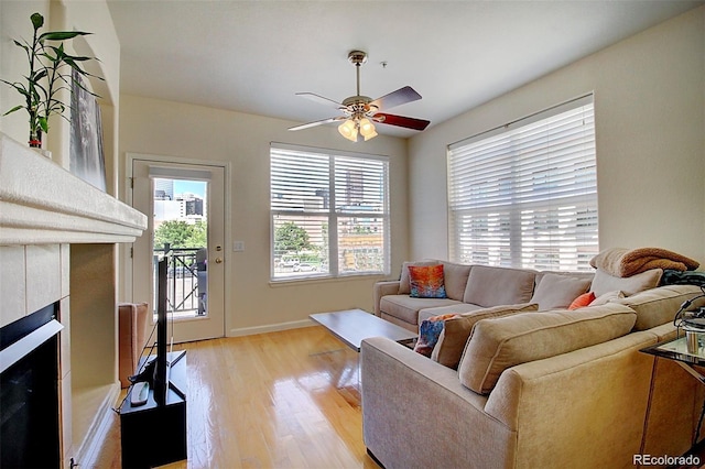 living area with a fireplace, light wood-style flooring, baseboards, and ceiling fan