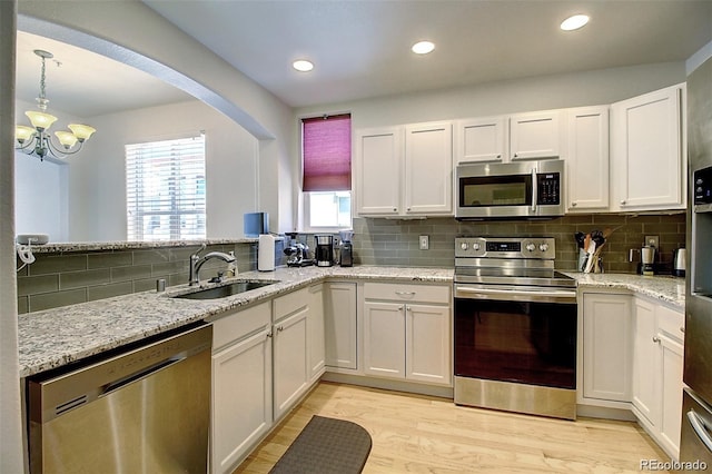 kitchen featuring appliances with stainless steel finishes, white cabinets, a sink, light stone countertops, and light wood-type flooring