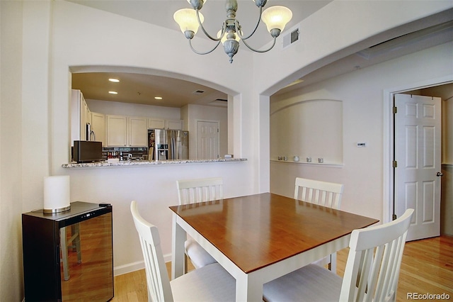 dining space featuring arched walkways, light wood finished floors, a chandelier, and visible vents