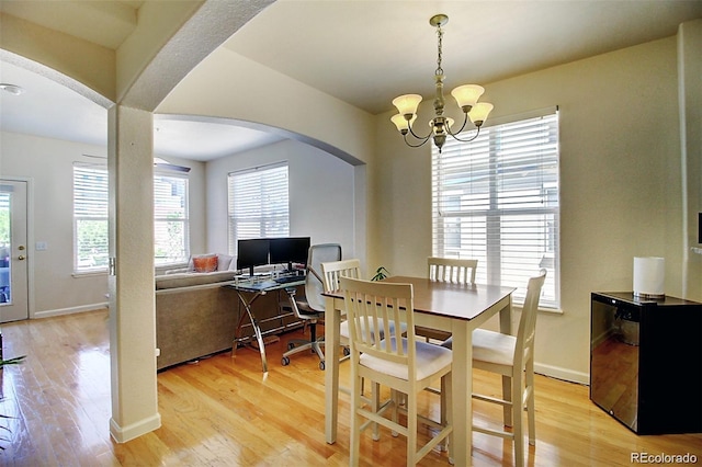 dining space featuring light wood-style floors, arched walkways, a notable chandelier, and baseboards