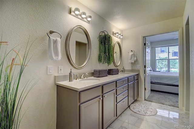 bathroom with a textured wall, marble finish floor, double vanity, and a sink