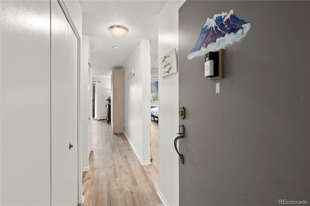 corridor featuring light wood-style floors, baseboards, and a textured ceiling