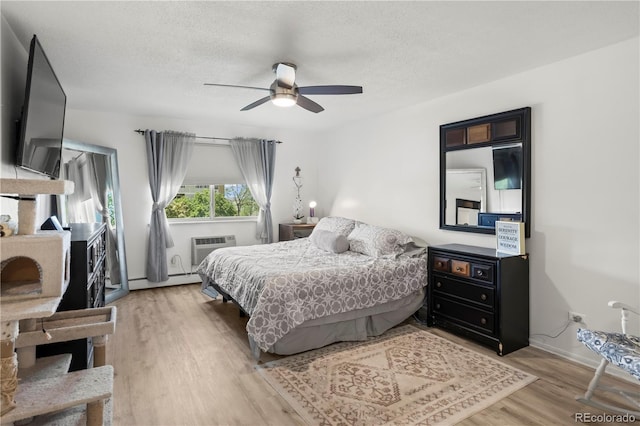 bedroom featuring wood finished floors, a textured ceiling, a wall mounted air conditioner, ceiling fan, and baseboards