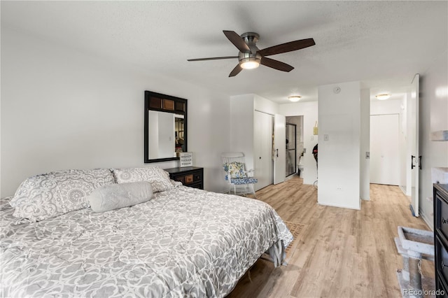 bedroom featuring light wood-style flooring, a textured ceiling, and a ceiling fan