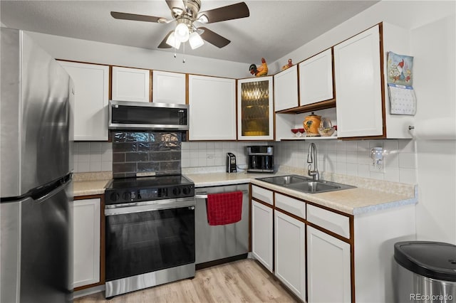kitchen featuring stainless steel appliances, a sink, light countertops, light wood-style floors, and backsplash