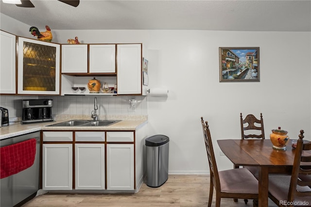 kitchen featuring stainless steel dishwasher, a sink, backsplash, light countertops, and light wood-style flooring