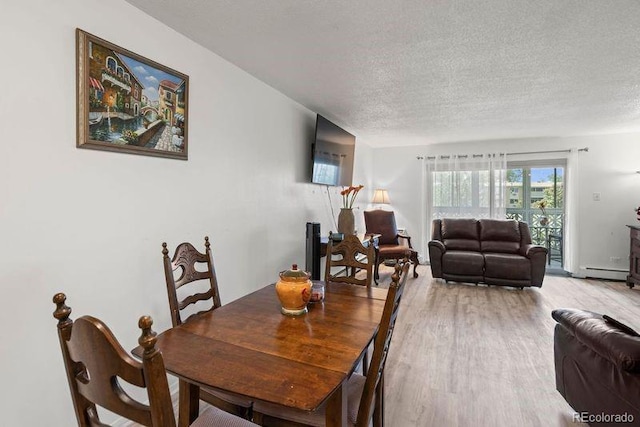 dining space featuring light wood-type flooring, a baseboard heating unit, and a textured ceiling