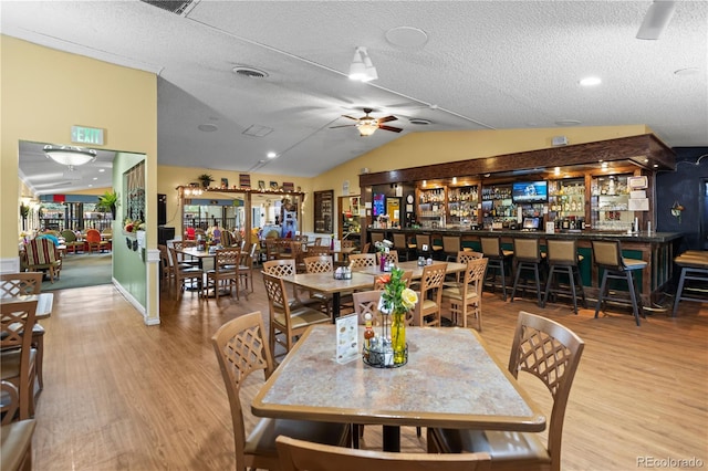 dining area with wood finished floors, lofted ceiling, a ceiling fan, and a textured ceiling