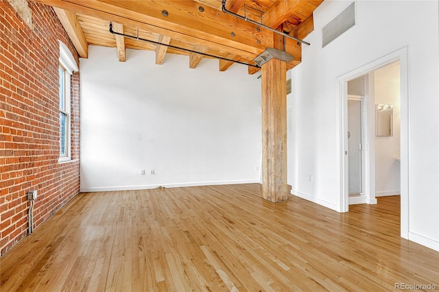 unfurnished room featuring beam ceiling, light hardwood / wood-style flooring, wooden ceiling, and brick wall