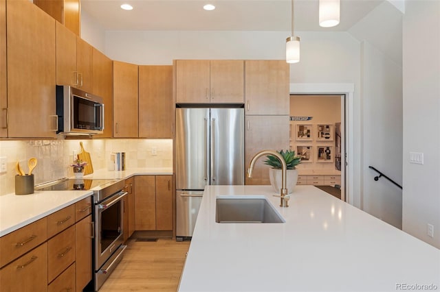 kitchen featuring pendant lighting, sink, light hardwood / wood-style flooring, decorative backsplash, and appliances with stainless steel finishes