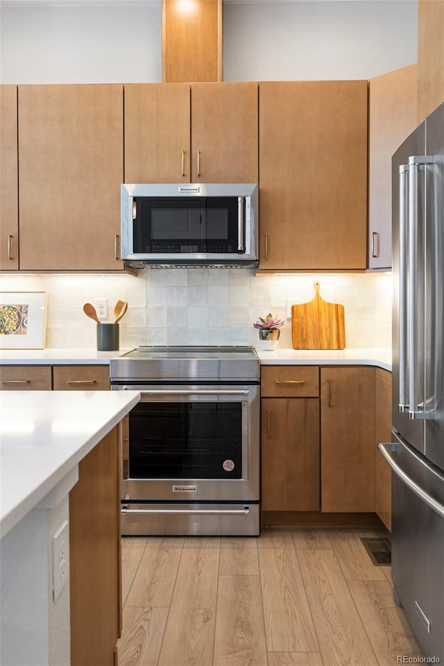 kitchen with light wood-type flooring, stainless steel appliances, and tasteful backsplash