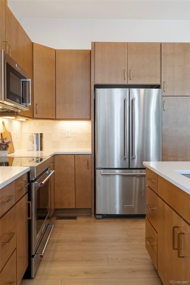 kitchen with light wood-type flooring, backsplash, and appliances with stainless steel finishes