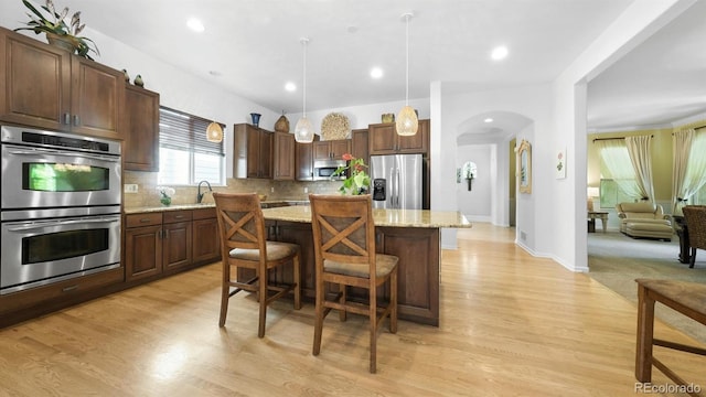 10328 Bluffmont Dr, Lone Tree, CO 80124 - kitchen featuring appliances with stainless steel finishes, a center island, tasteful backsplash, arched walkways, and light wood finished floors